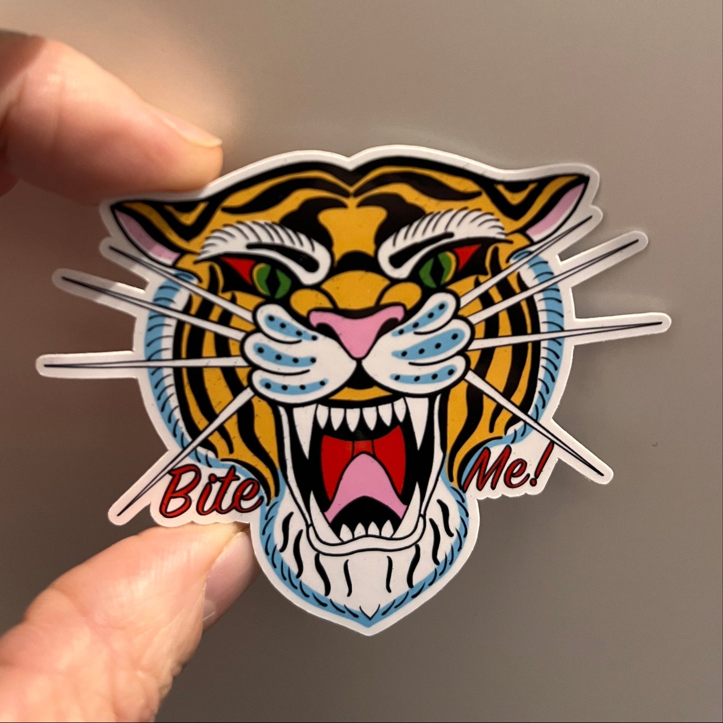 Colorful tiger sticker held between fingers against a neutral background