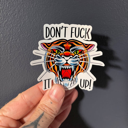 Sticker with a tiger design and text held by a hand against a dark background