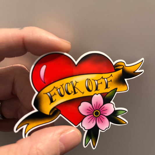 Sticker with red heart and yellow banner with 'F*ck Off', and pink flower held between fingers against a neutral background