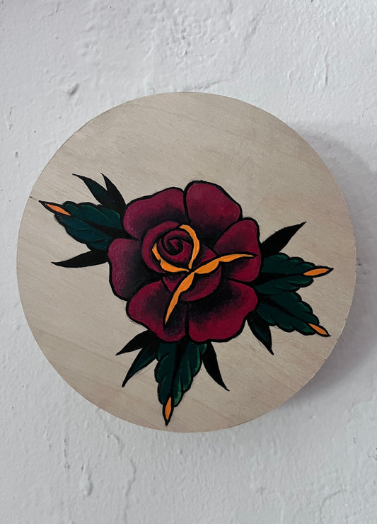 Wooden circular wood panel with a hand painted tattoo-style rose design on a white background