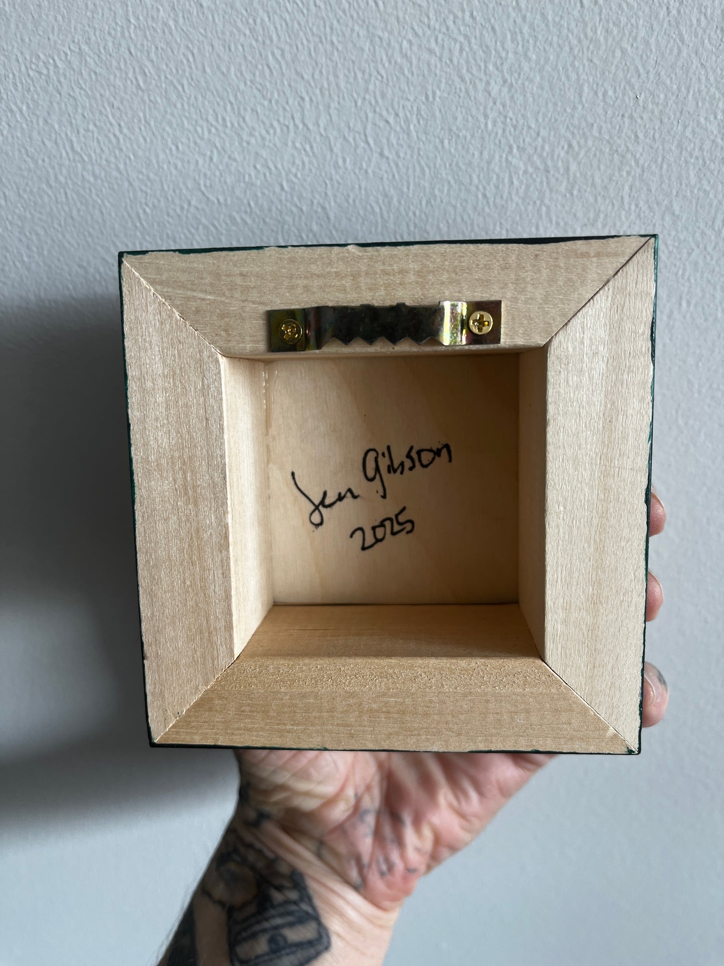 Hand holding a small wooden box with a signature and date on a gray background