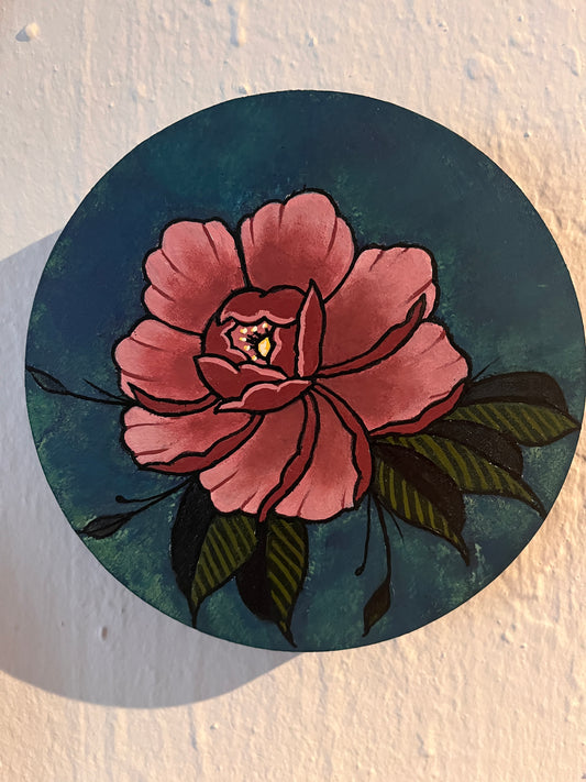 Close up view of a pink peony flower design on a wood panel photographed on textured white surface