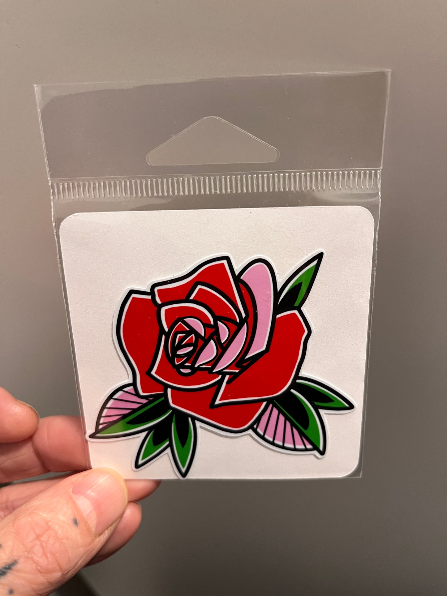 Hand holding a clear plastic card with a red rose sticker.