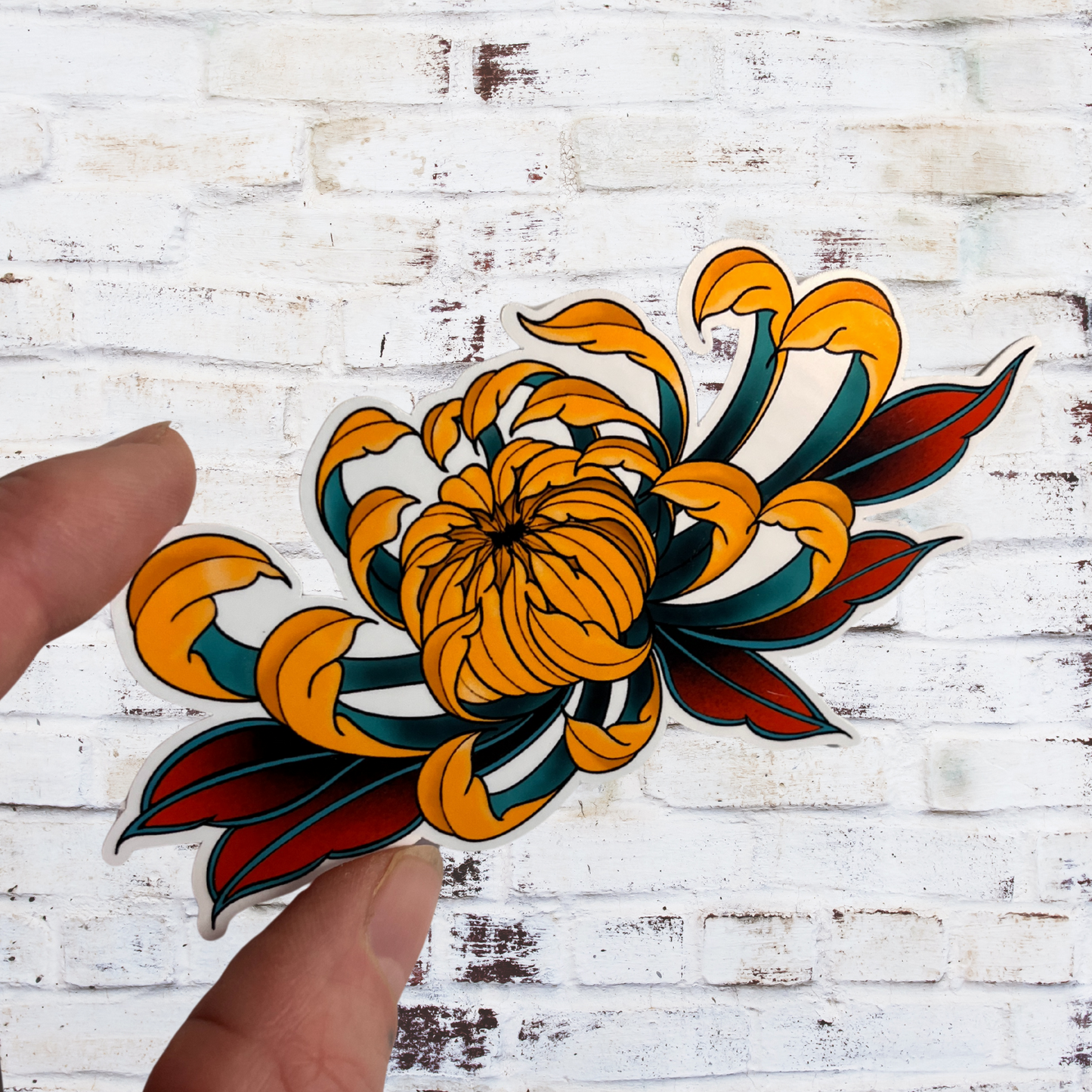 Colorful tattoo-style flower design held by a hand against a white wooden background