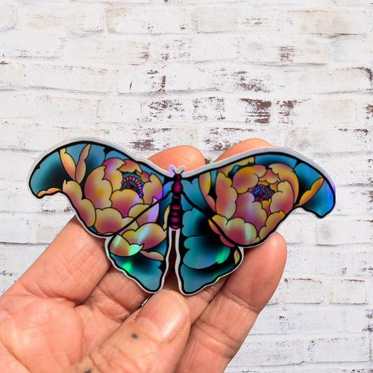 Colorful butterfly-shaped sticker held by a hand against a wooden background