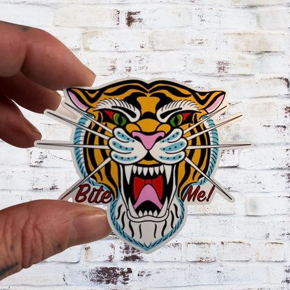 Sticker of a tiger with the text 'Bite Me!' held against a wooden background