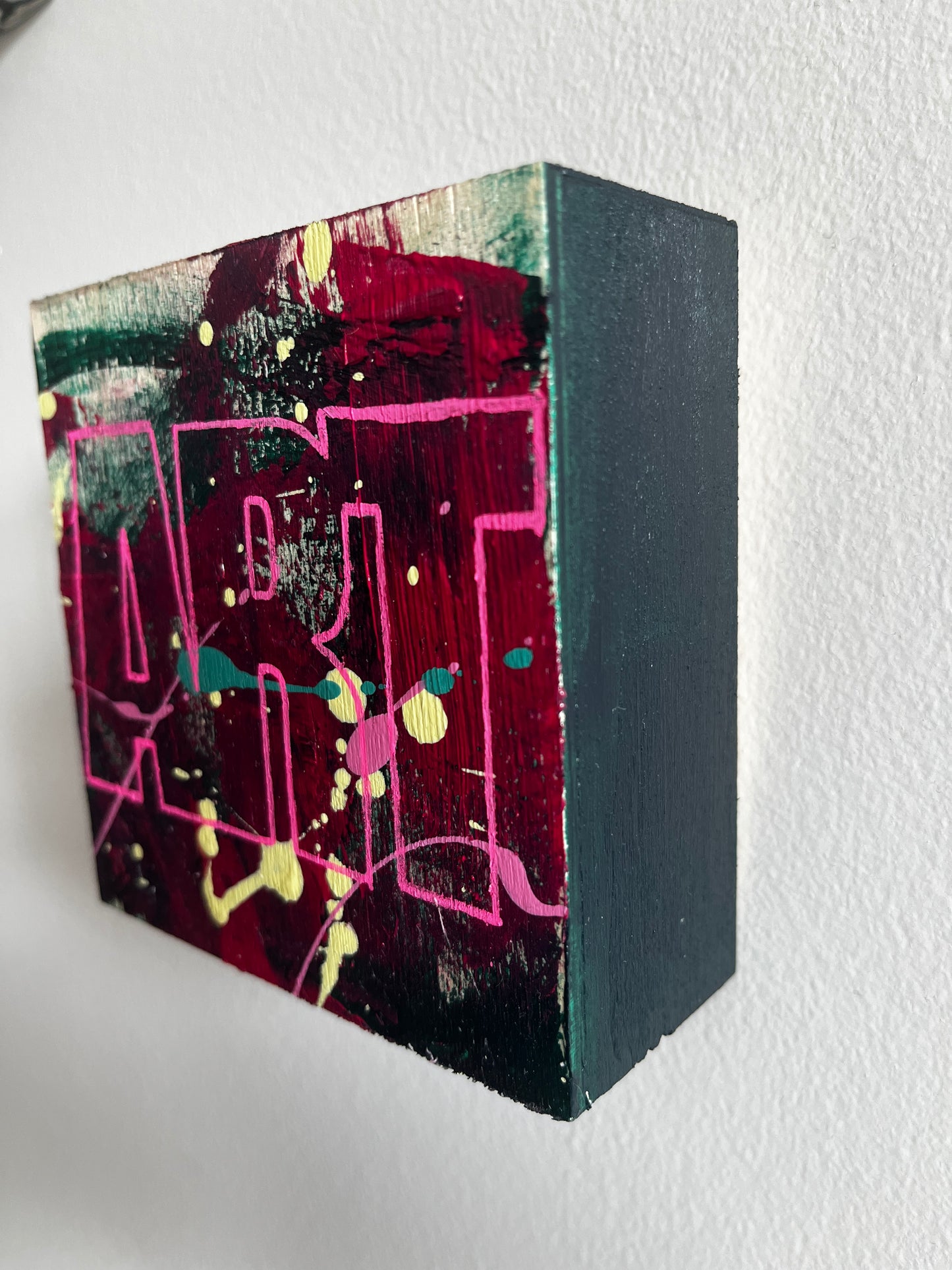 Abstract art piece on a rectangular block with black, pink, and multicolor design.