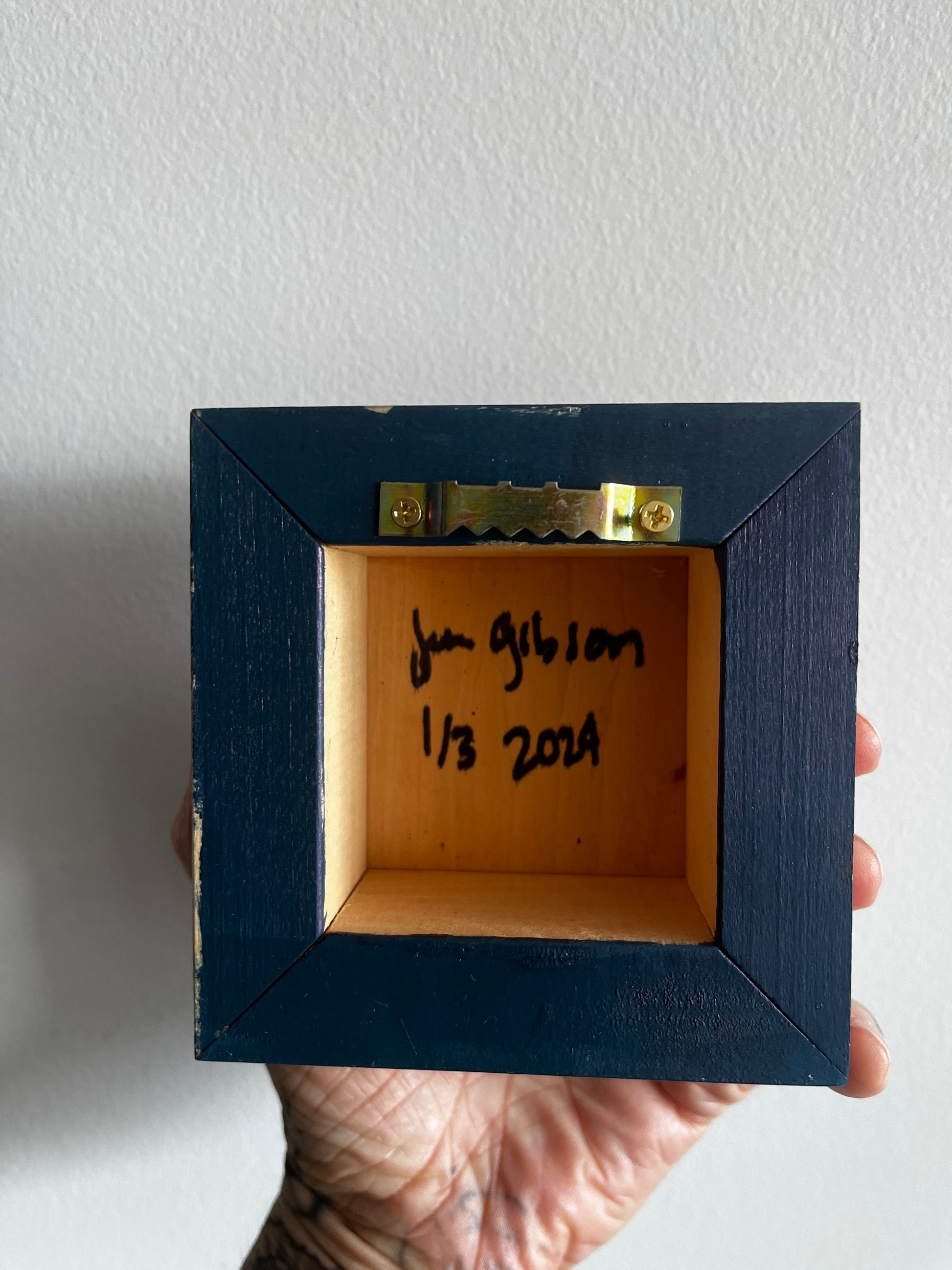 Hand holding a small wooden box with a blue frame against a white background