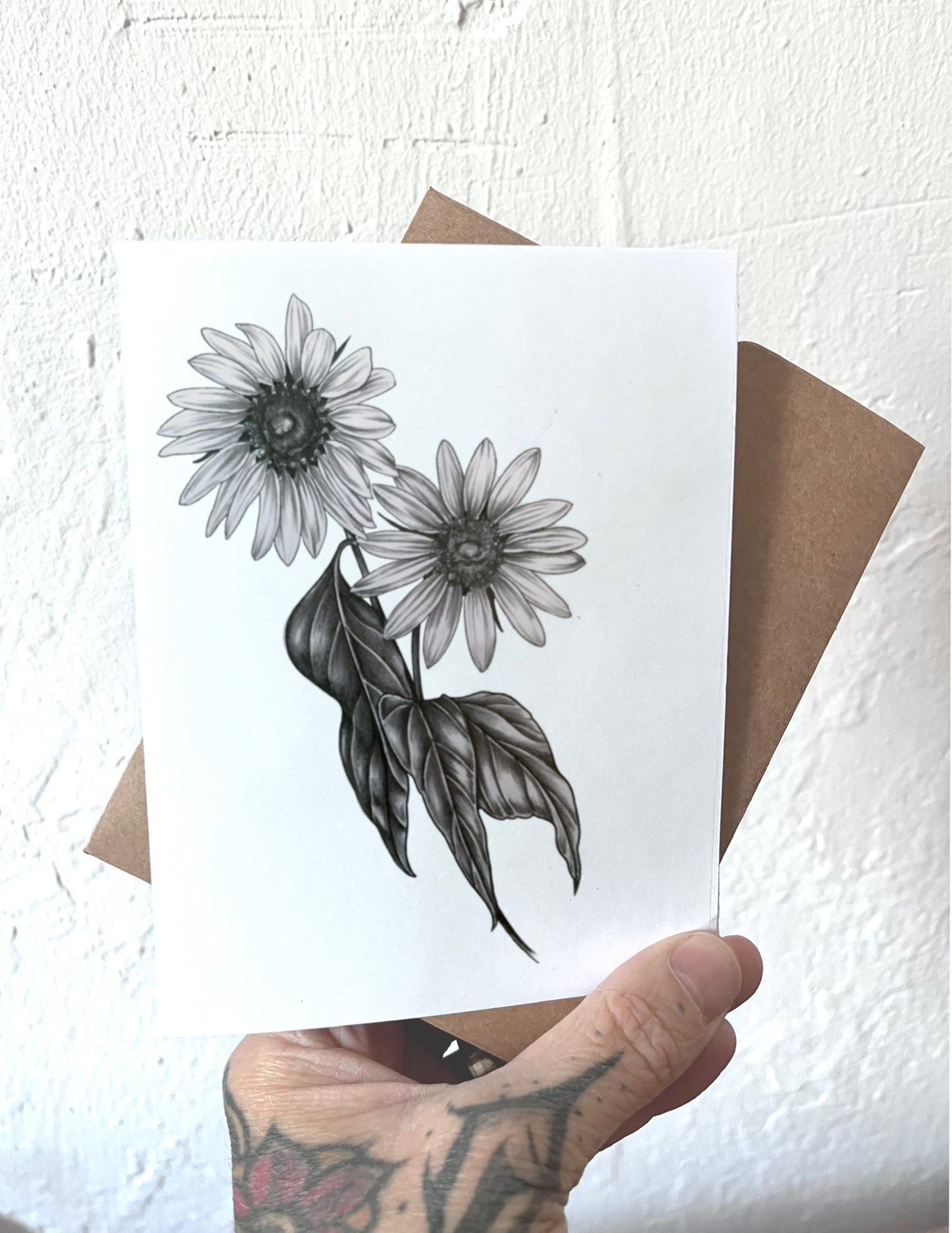 Hand holding a card with black and white floral design against a textured white background