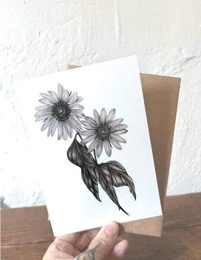 Card with black and white floral design held by a hand on a wooden surface.