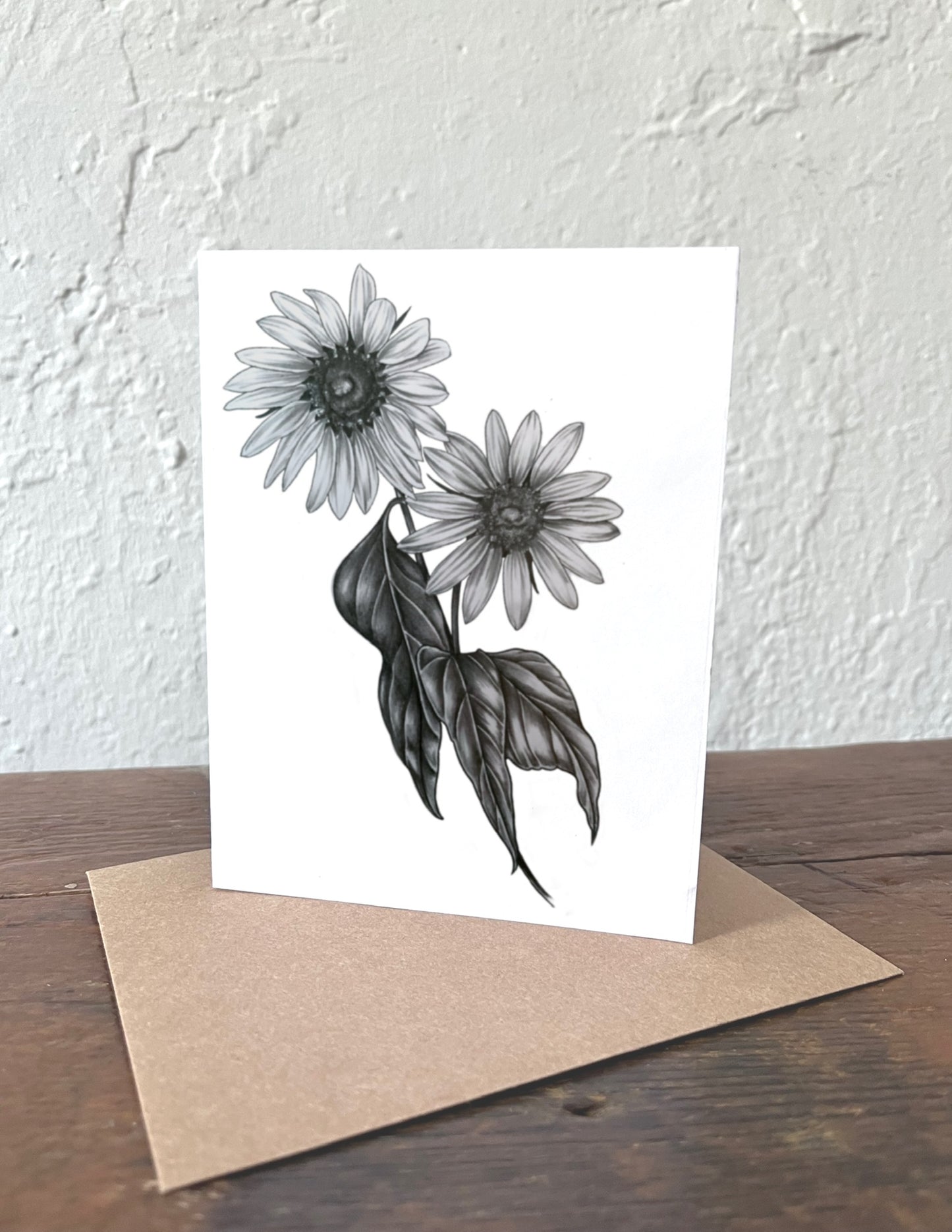 Greeting card with black and white floral design on a wooden surface with a beige envelope.