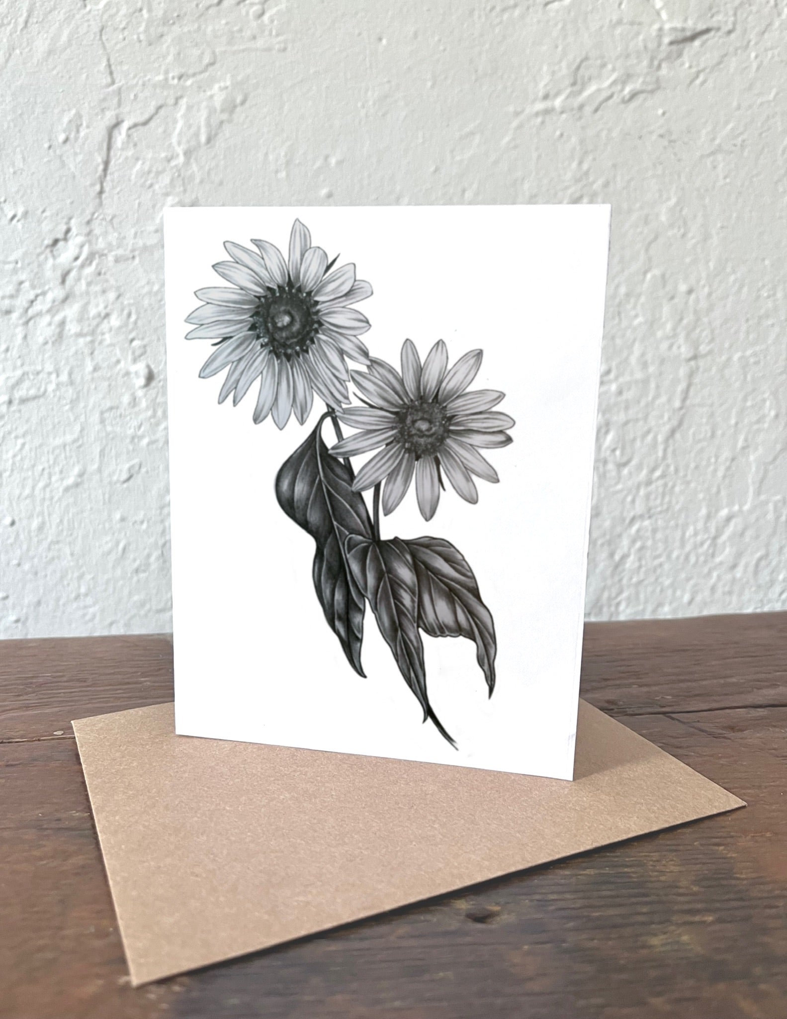 Greeting card with black and white floral design on a wooden surface with a beige envelope.
