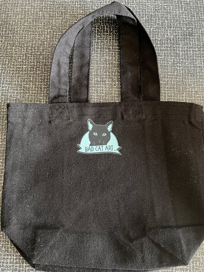 Black tote bag with a cat graphic and text on a textured surface
