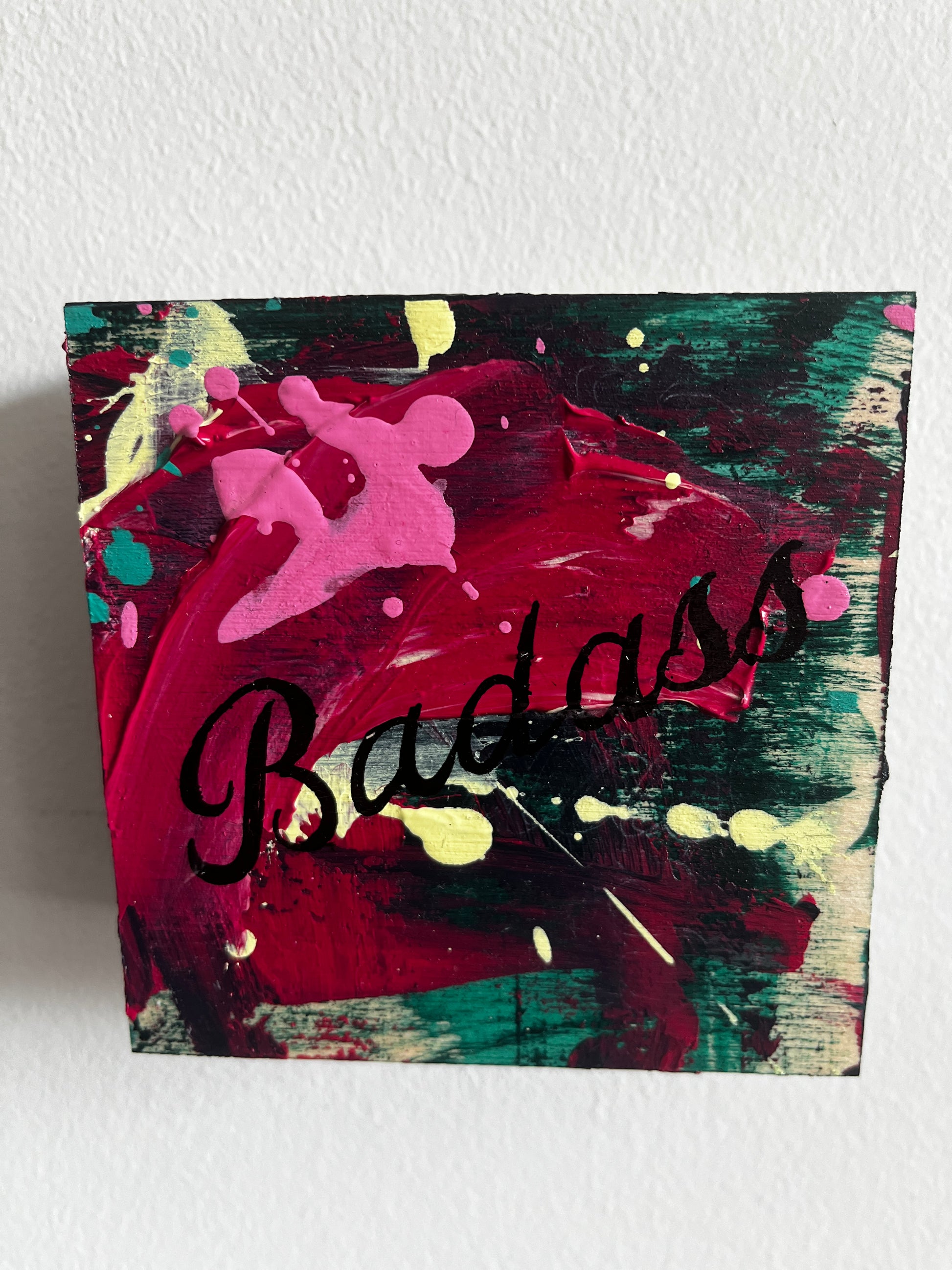 Abstract painting with Black badass text on a textured white wall 