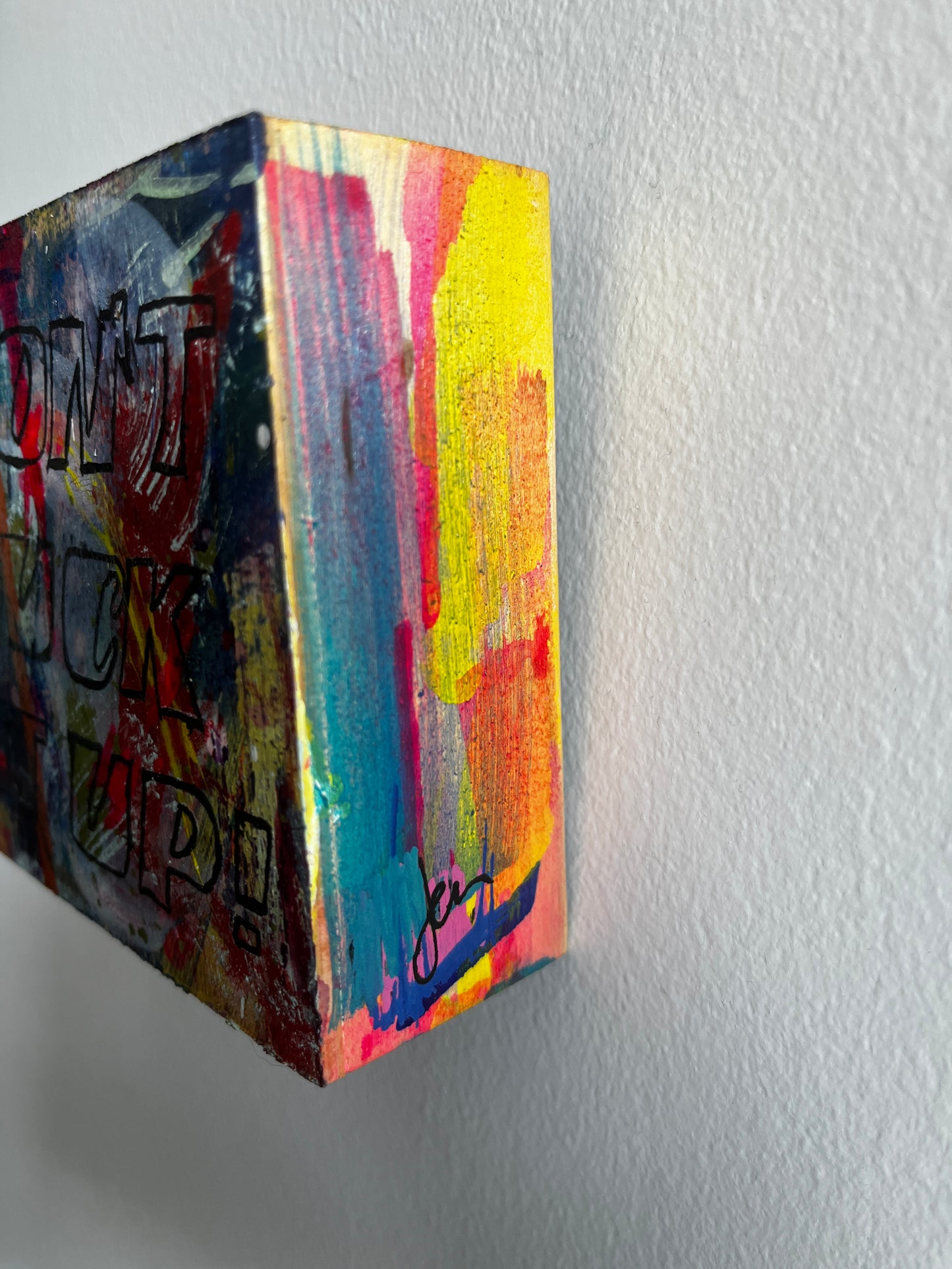Colorful abstract painting on a wooden block against a plain background