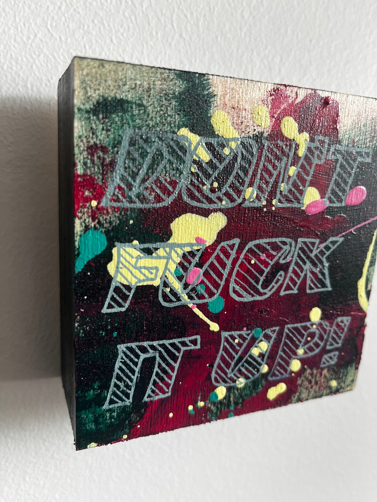 Wooden art with colourful abstract design & text on a white background