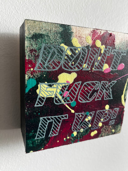 Wooden art with colourful abstract design & text on a white background