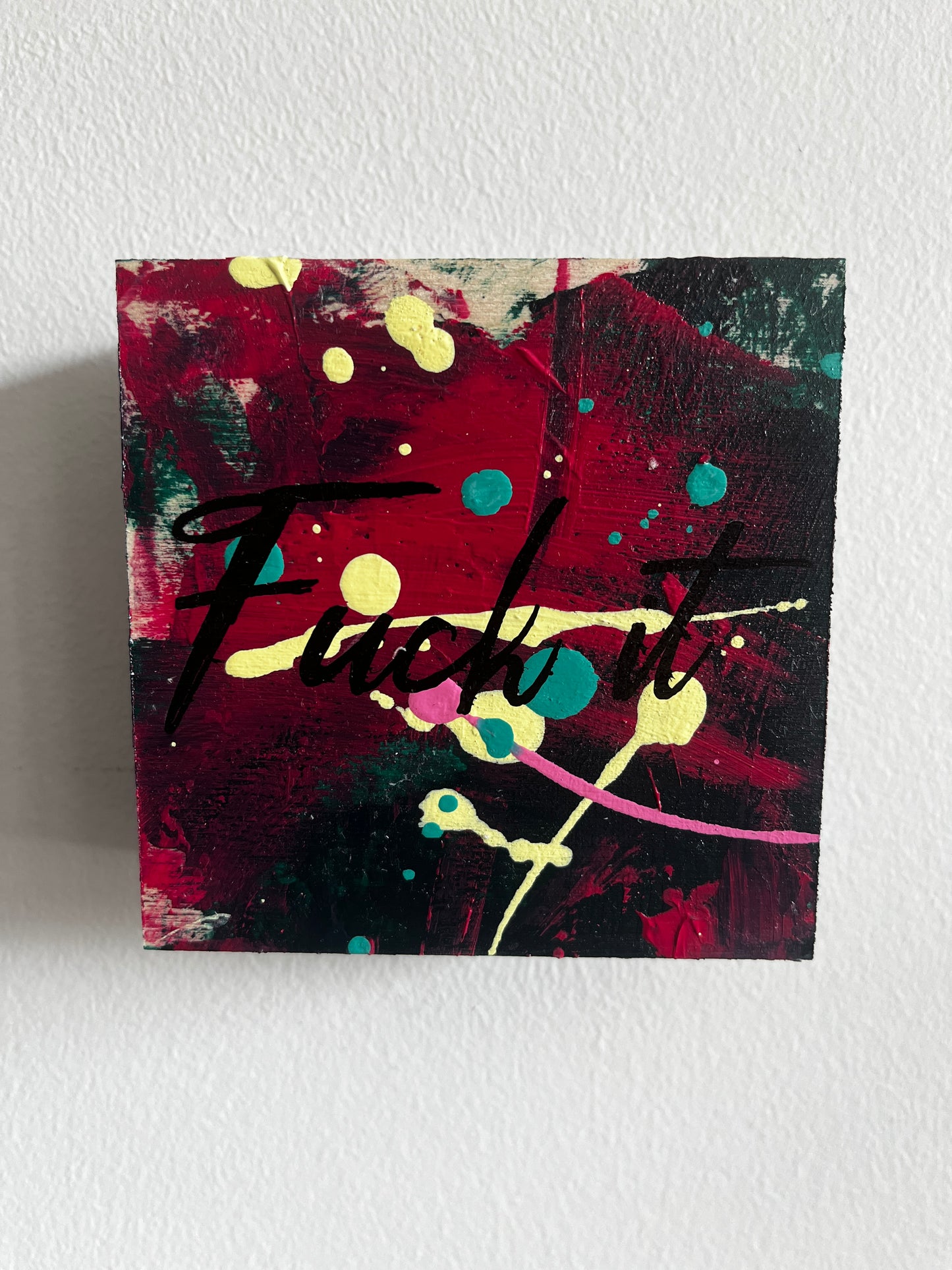 Abstract painting with splashes of red, yellow, and black on a white wall.