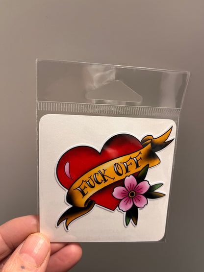 Tattoo-style design with a heart, banner, and flower held in a clear plastic sleeve.