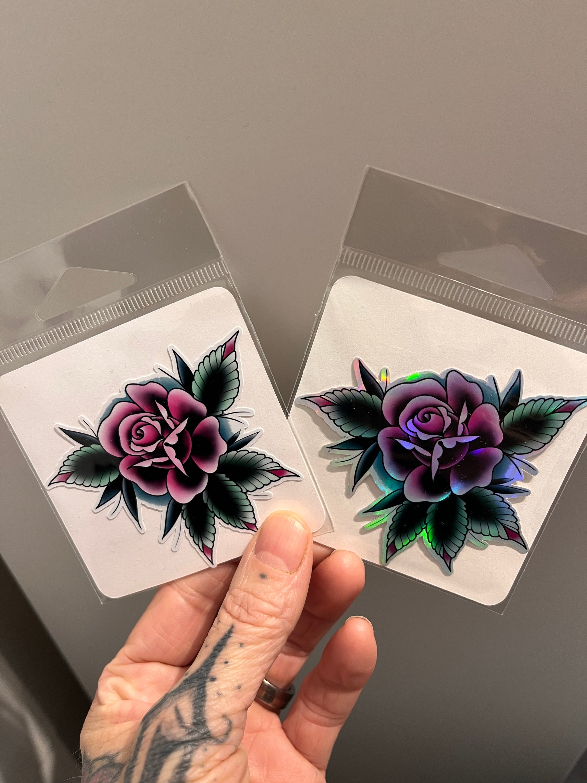 Hand holding two stickers with floral designs in protective packing