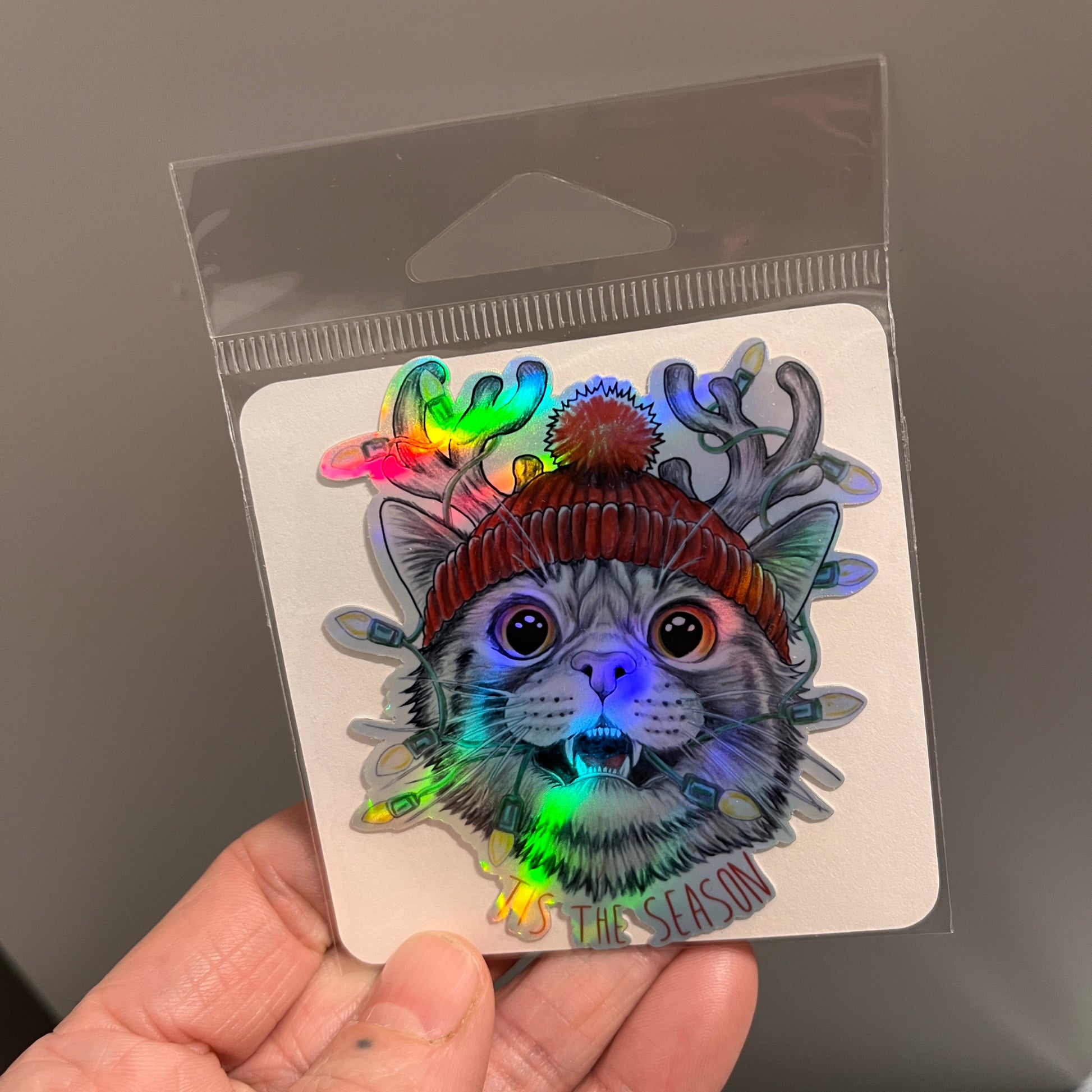 Holographic sticker of a cat design held by a person against a neutral background