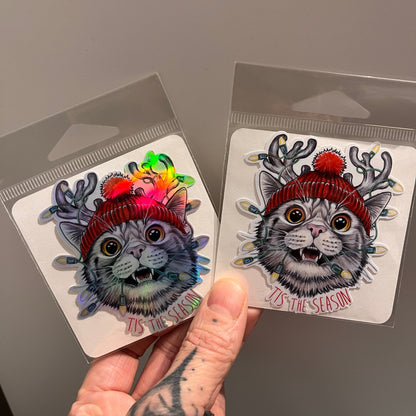 Two colorful cat-themed stickers held by a hand on a gray background
