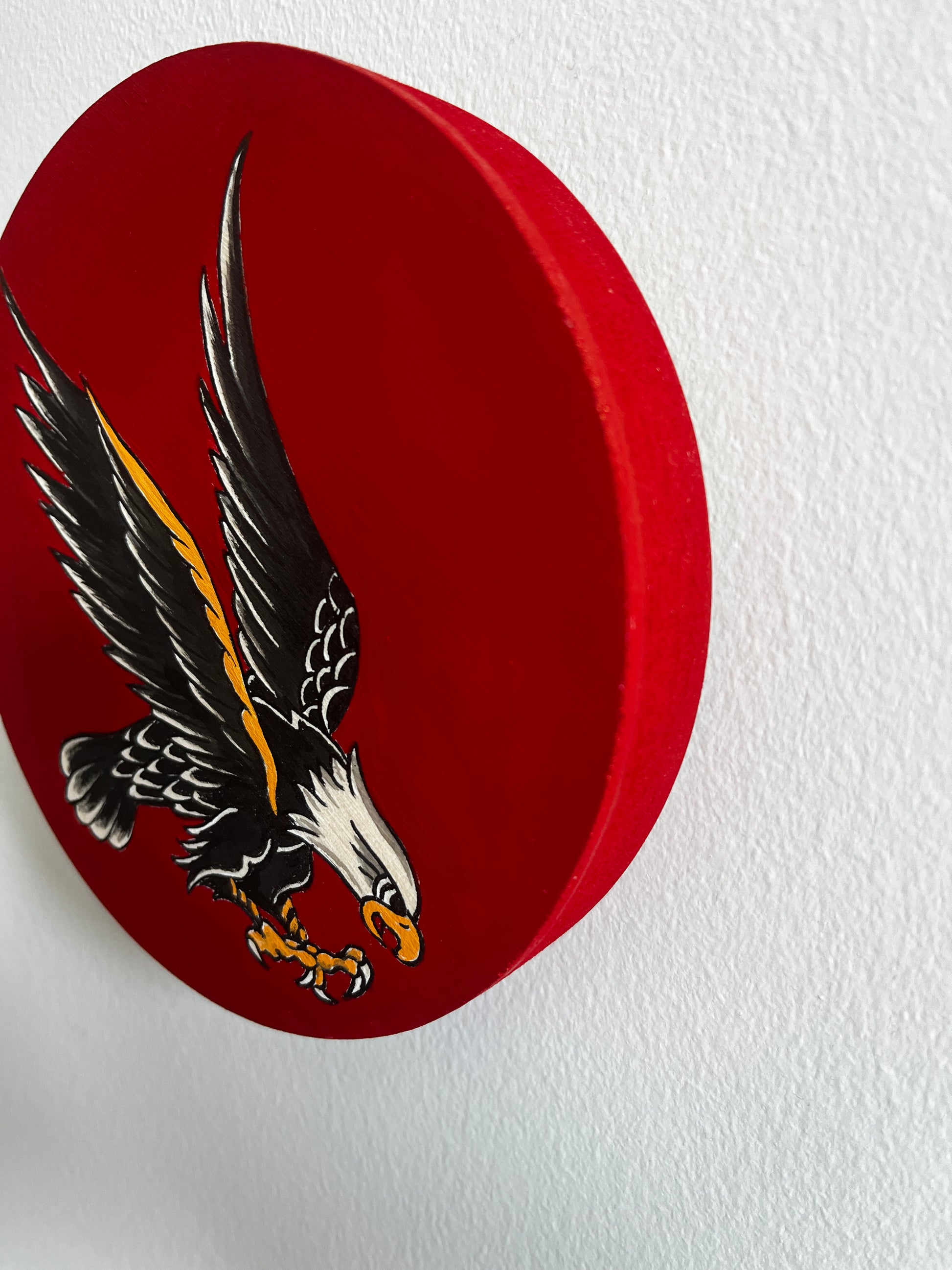 Red circular wooden art panel with an eagle emblem on a white background