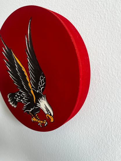 Red circular wooden art panel with an eagle emblem on a white background