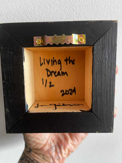 Black picture frame with 'Living the Dream 1/2 2024' written inside, held by a person.