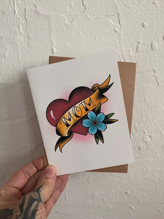 Card with 'Mom' design held by a hand against a white wall