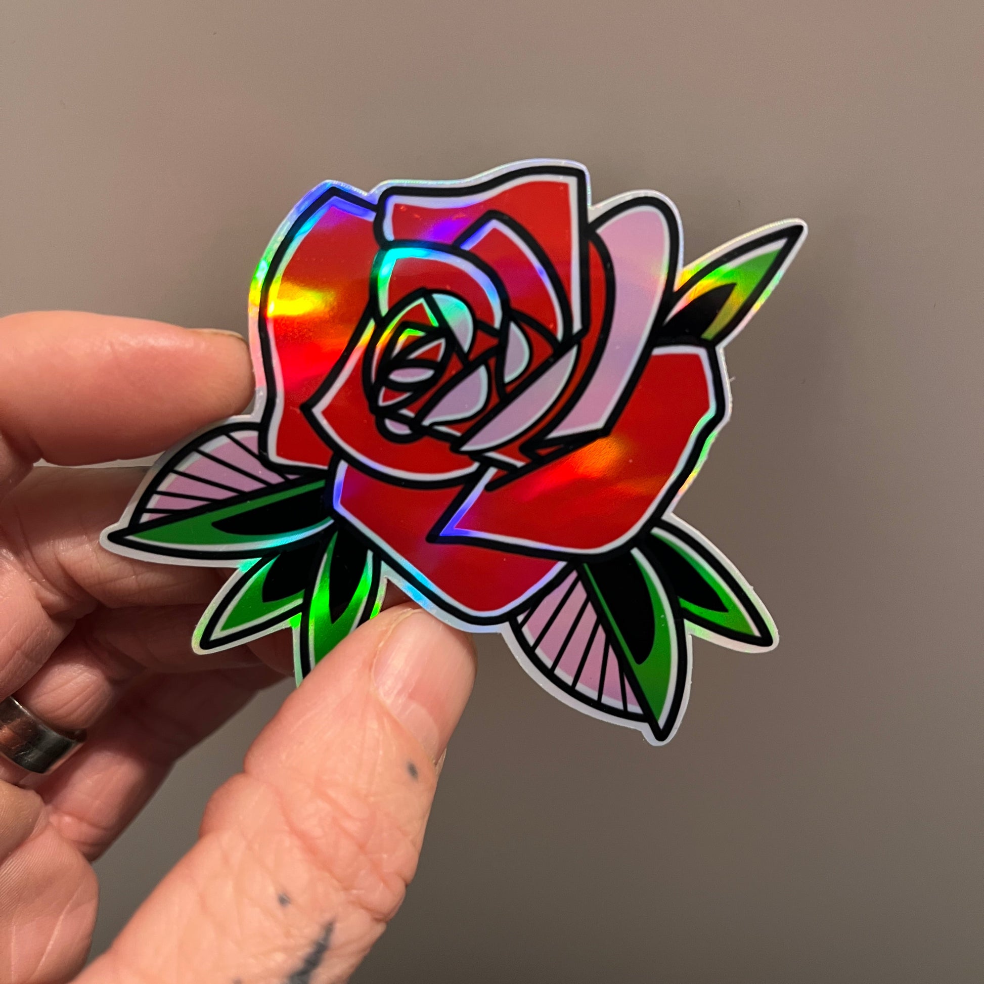 Holographic rose sticker held between fingers against a neutral background