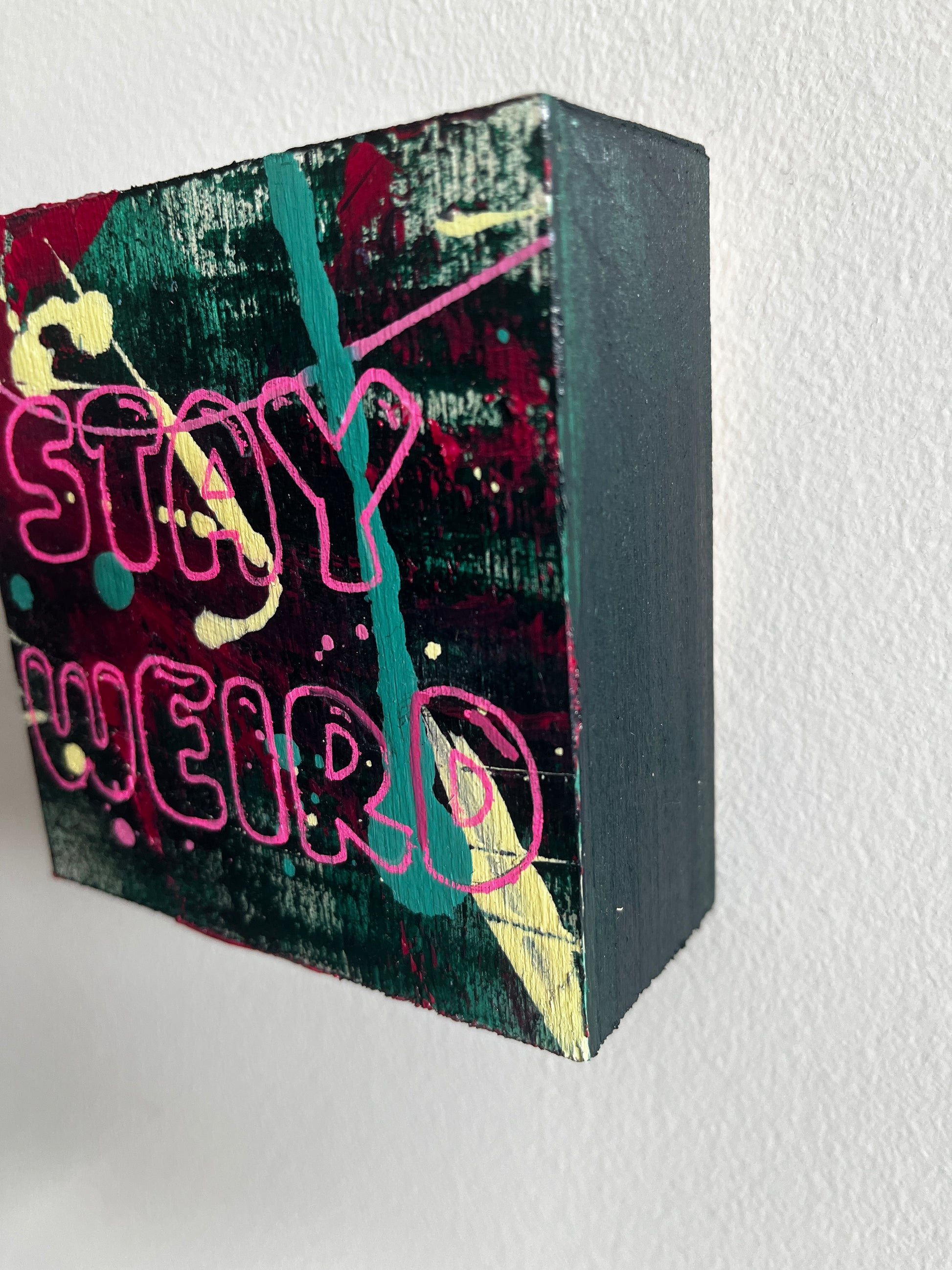 Black rectangular block with colorful graffiti-style text and designs on a light gray background