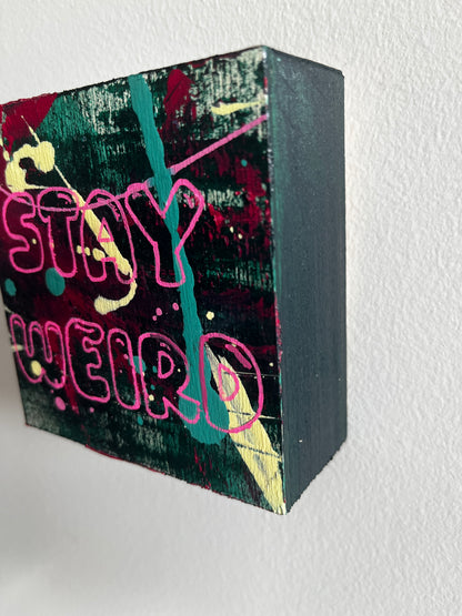 Black rectangular block with colorful graffiti-style text and designs on a light gray background