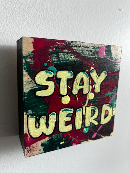Colorful block painting with 'Stay Weird' text on a white background