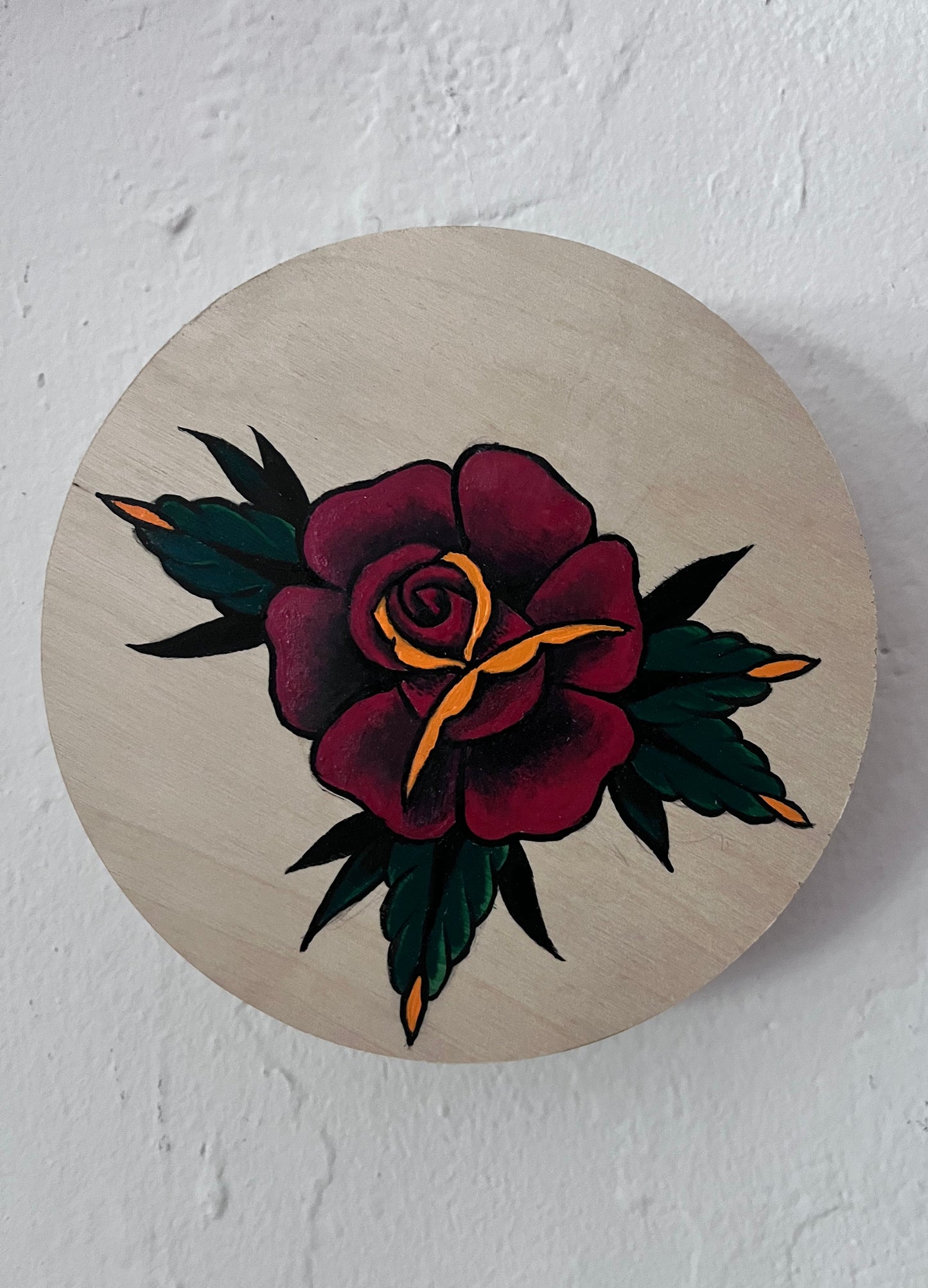 Wooden circular wood panel with a hand painted tattoo-style rose design on a white background