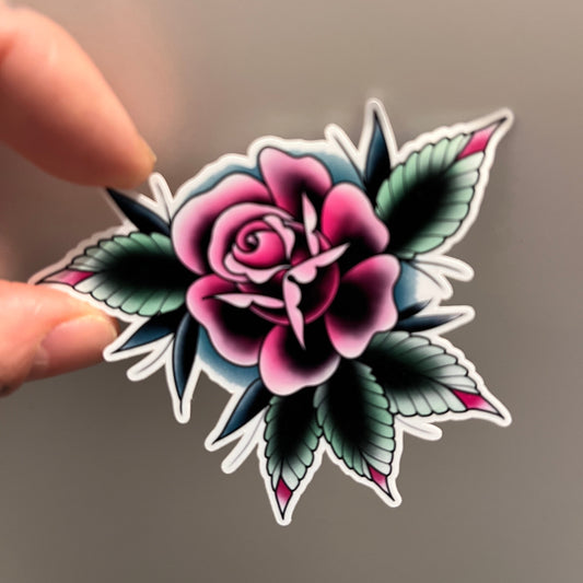 Decorative sticker of a pink rose with green leaves held by a hand against a neutral background