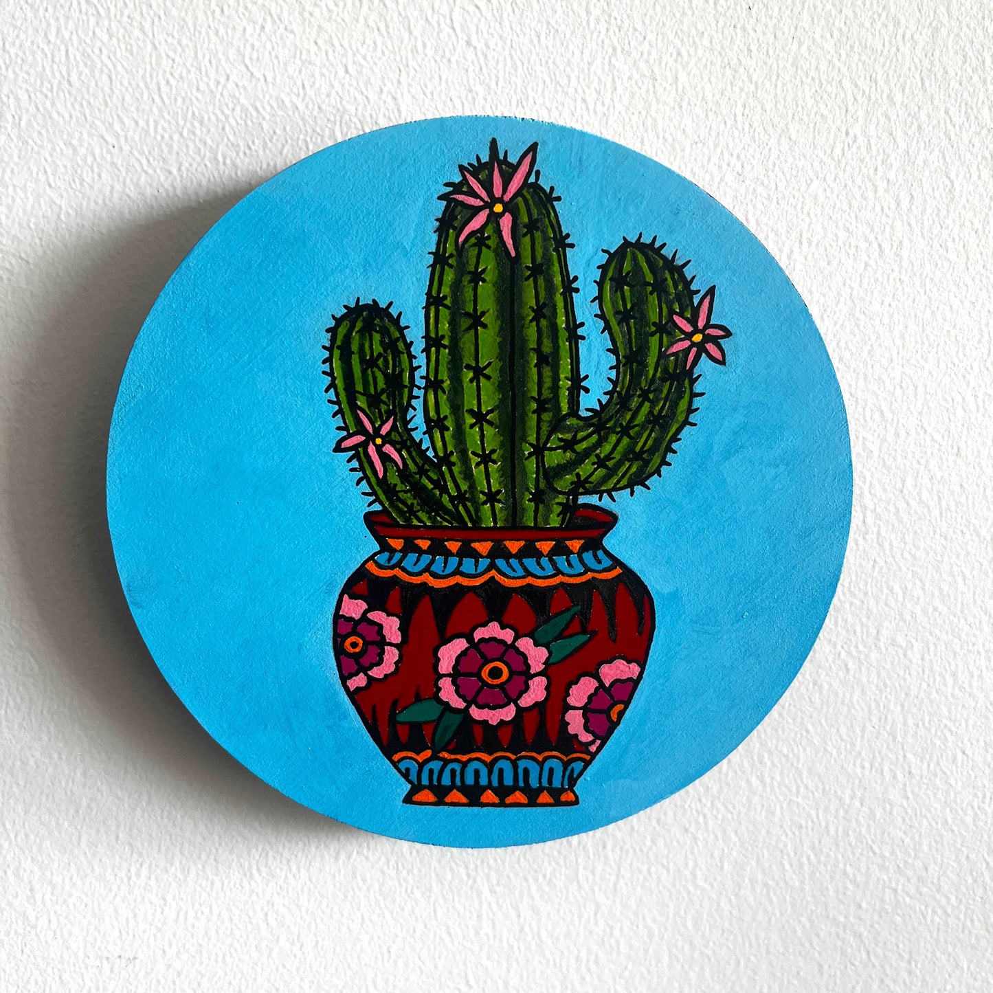 Circular painting with a cactus in a fancy pot design on a blue background