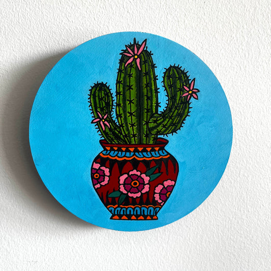 Circular painting with a cactus in a fancy pot design on a blue background
