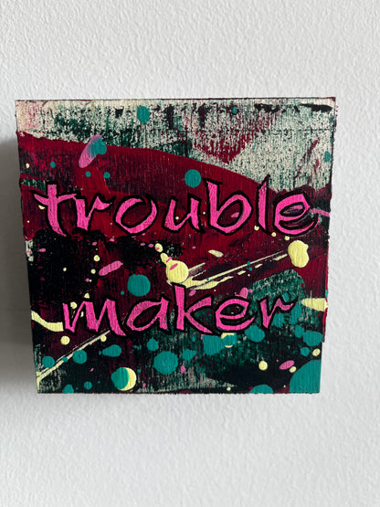Colourful abstract design and text saying Trouble maker on a light grey background