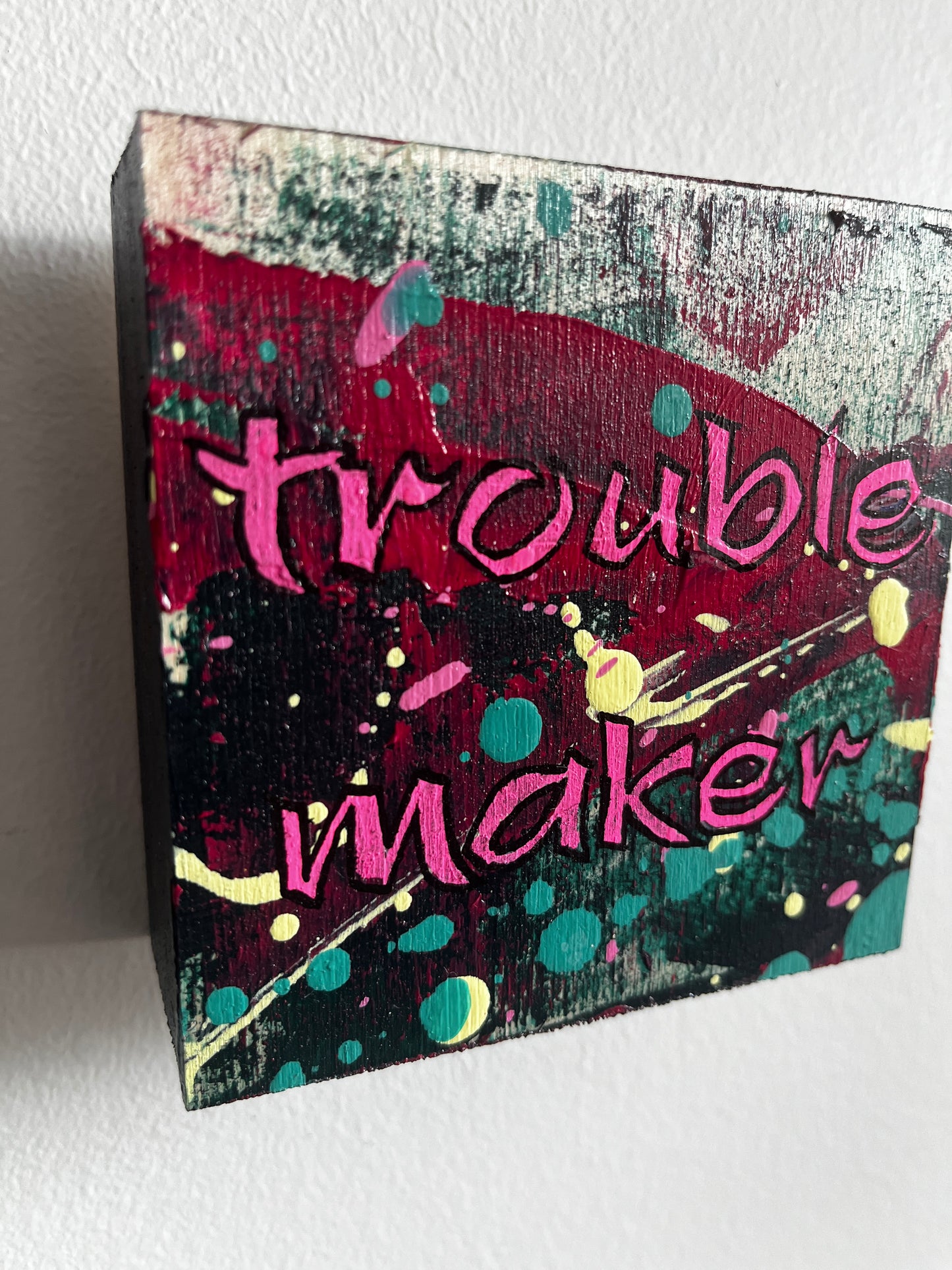 Abstract square painting with 'trouble maker' text and colourful design on a white background