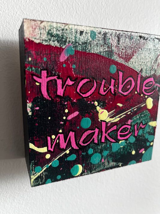 Abstract square painting with 'trouble maker' text and colourful design on a white background