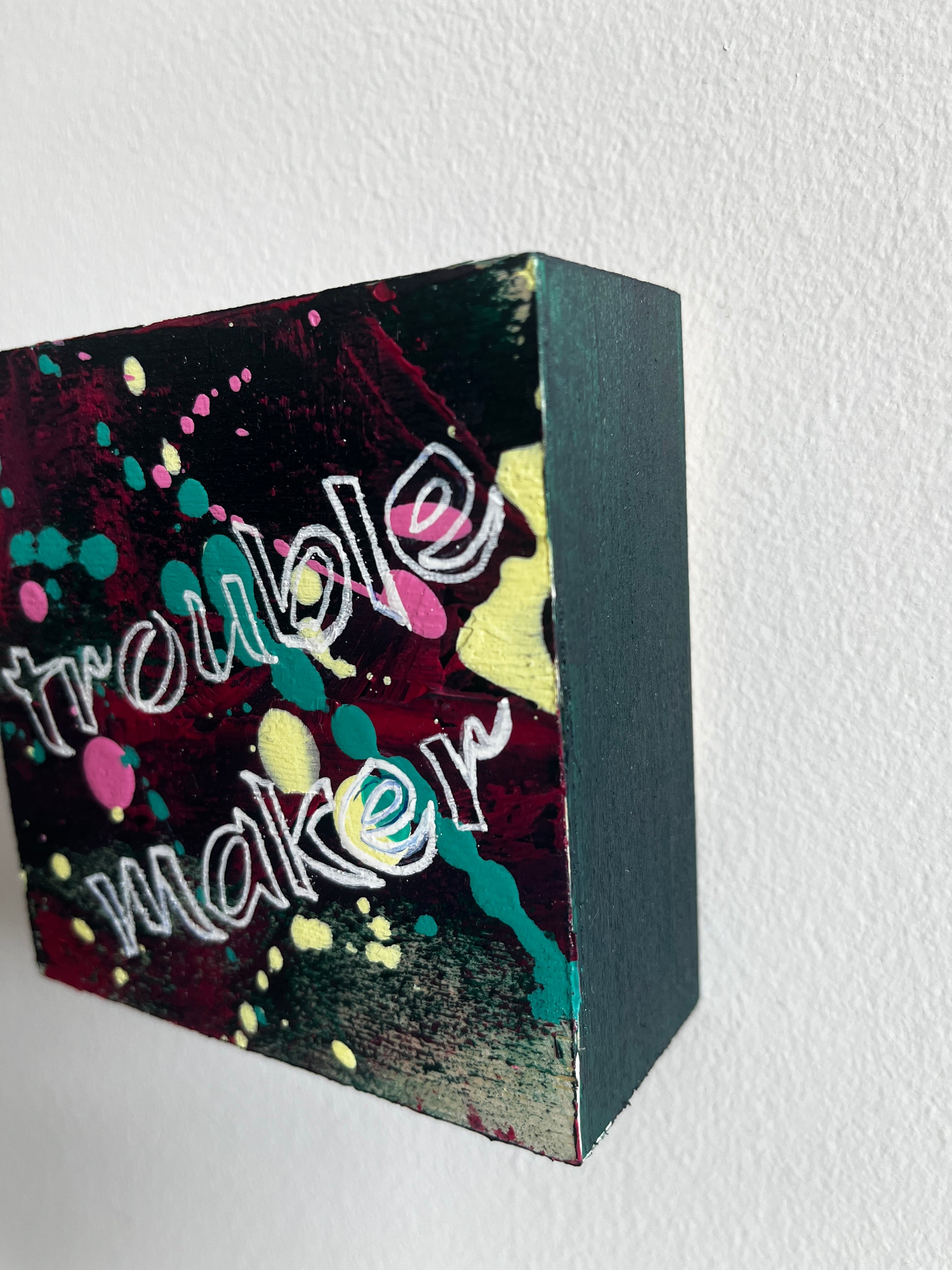 Square art with colourful abstract design and 'Trouble Maker' text on a white background