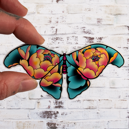 Colorful butterfly-shaped sticker held by a hand against a white brick background