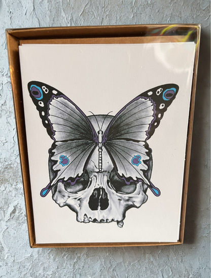 Card with a butterfly design on a skull, placed inside a box on a textured surface.