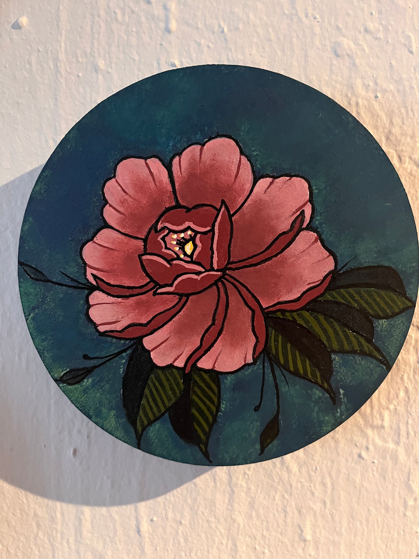 Close up view of a pink peony flower design on a wood panel photographed on textured white surface