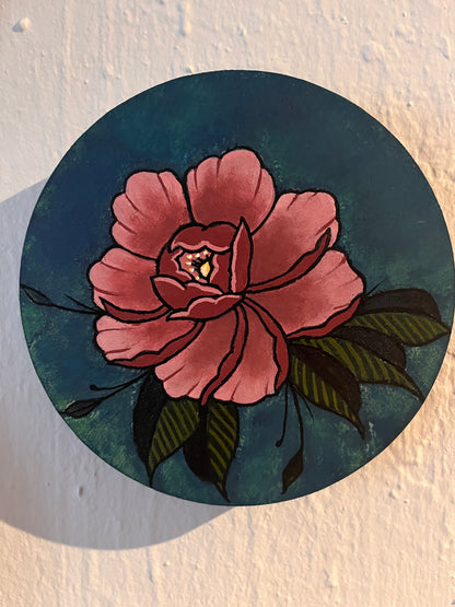 Close up view of a pink peony flower design on a wood panel photographed on textured white surface