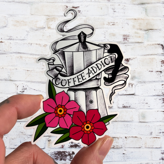 Sticker of a coffee pot with 'Coffee Addict' text and flowers held against a white brick wall.