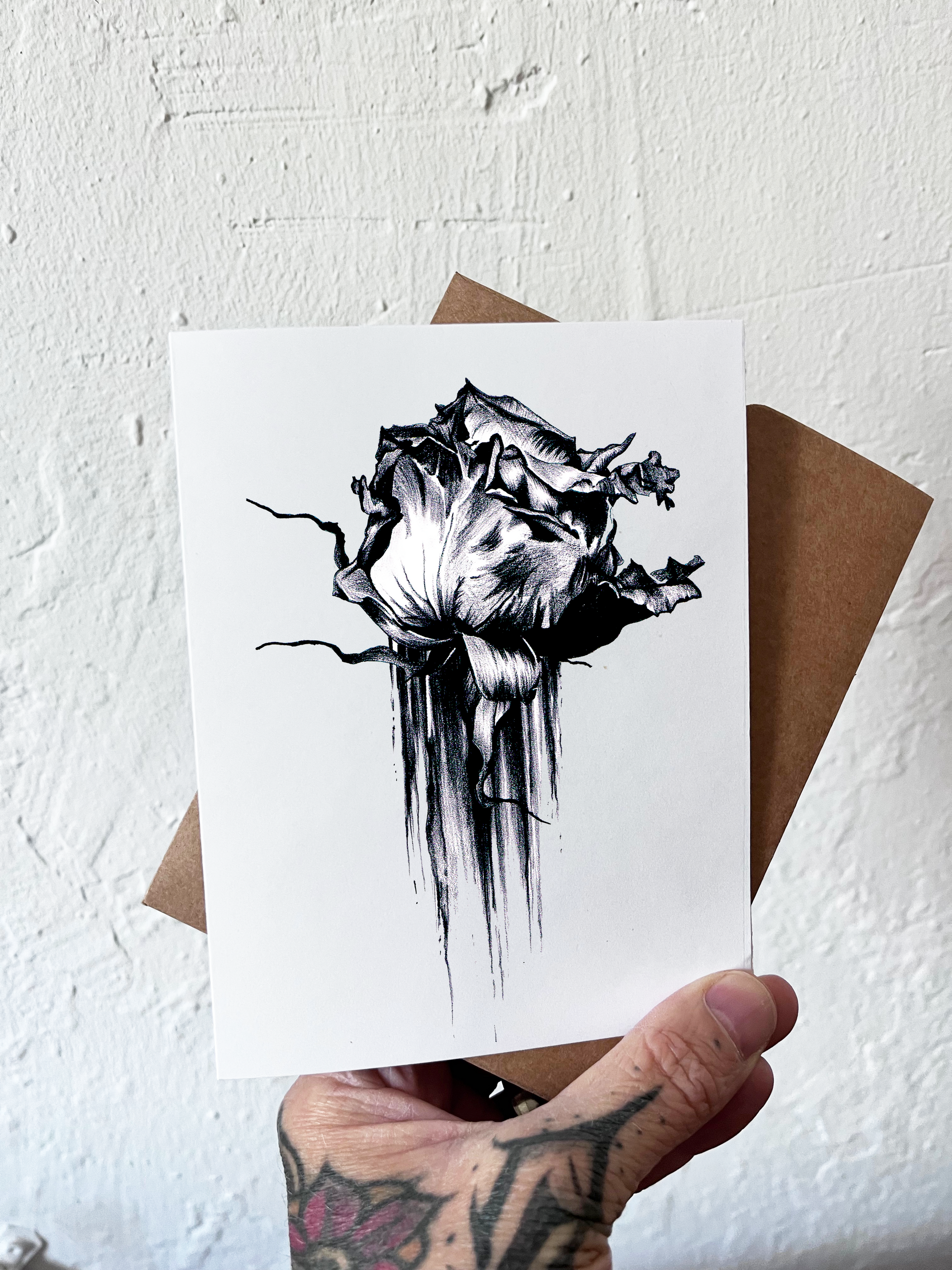 Greeting card with black and white floral design held by a hand against a textured white background