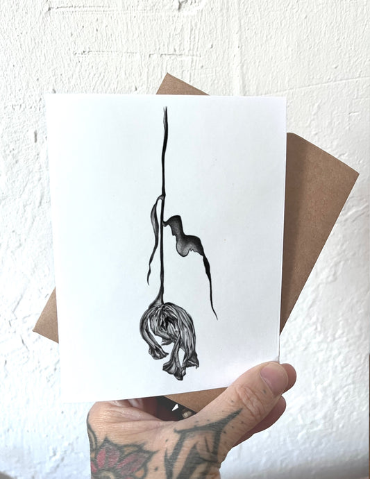 Hand holding a card with a black and white illustration of a dried tulip hanging upside down against a white background.