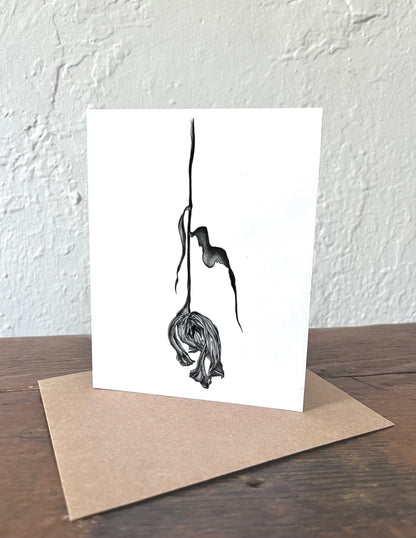 Greeting card with a black and white illustration of a dried tulip on a white background, placed on a wooden surface with a kraft envelope.